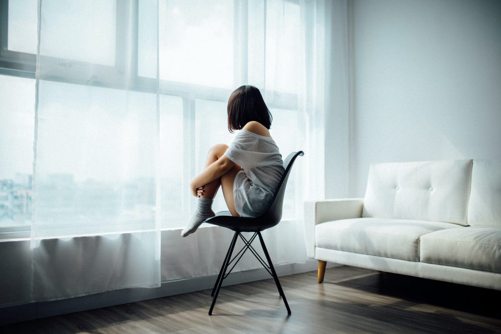 Eine Frau sitzt auf einem Stuhl allein in einem Zimmer und schaut zum Fenster hinaus